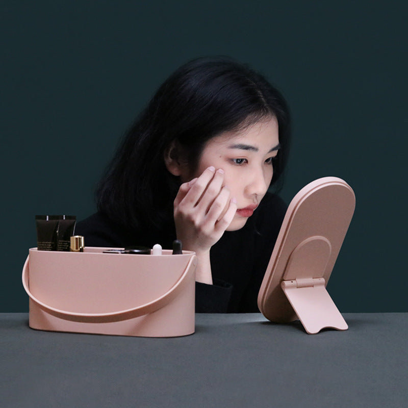 Woman applying makeup in front of a pink compact mirror on a dark background