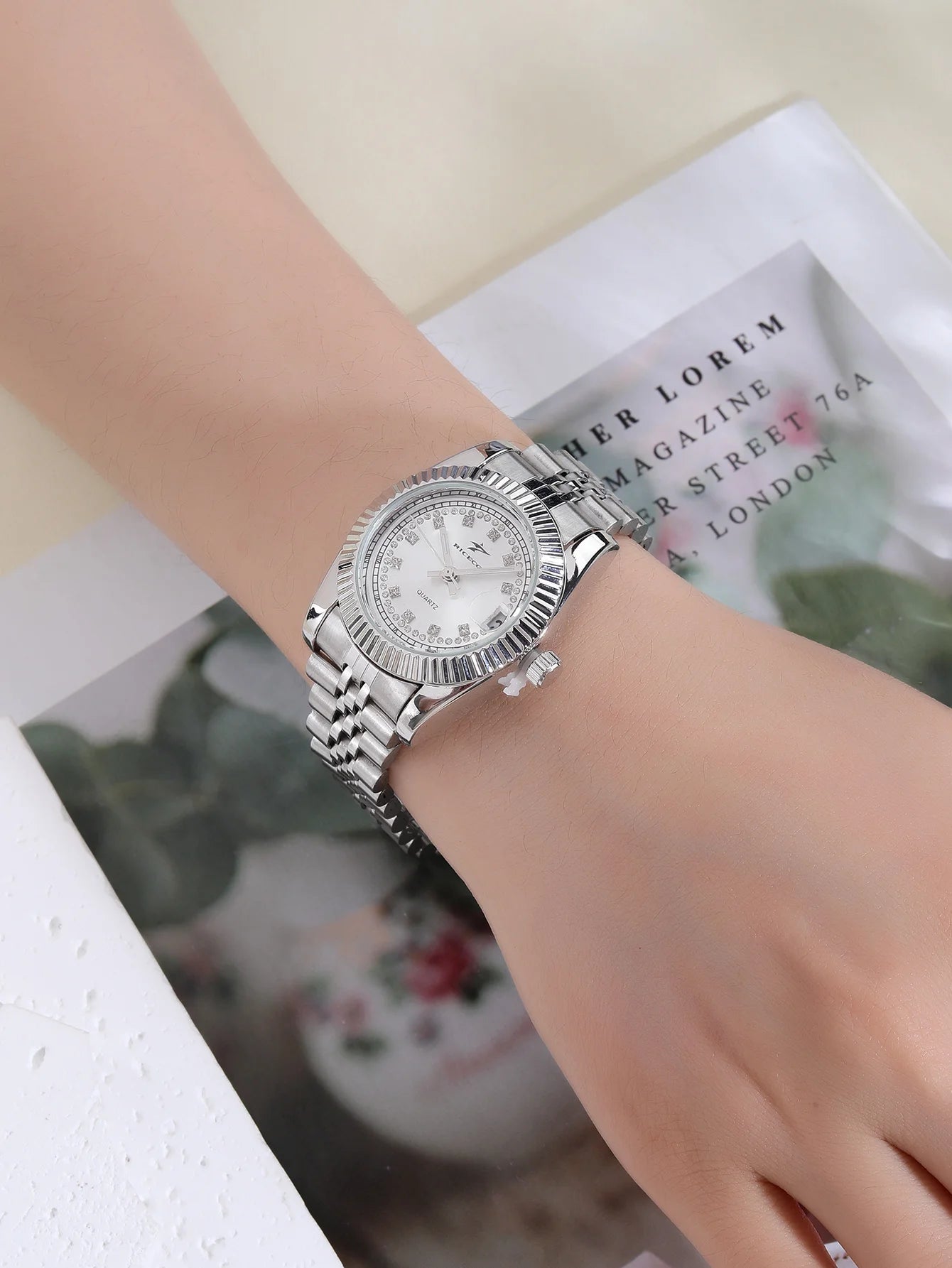 A women's quartz wristwatch with a textured bezel design and diamond studded dial decoration, equipped with date display functio